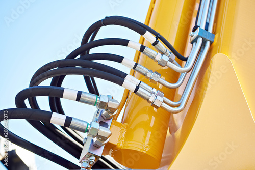 Hydraulic hose connections on yellow excavator cylinder
