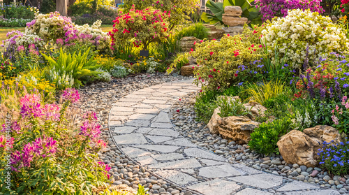 Fényképezés Beautiful winding stone paver path through a lush, vibrant garden blooming with colorful flowers and green plants