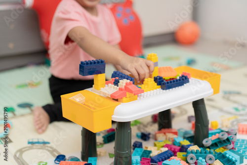 Child hand assembling colorful plastic building blocks on white toy table