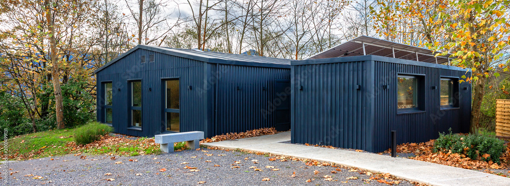 Fototapeta premium Banner of modern office building constructed from shipping containers, featuring solar panels, blending contemporary sustainable architecture with the surrounding autumn nature of forest