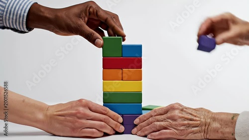 Two hands collaboratively build a colorful tower of square blocks, symbolizing teamwork, diversity, and progress against a clean white background.