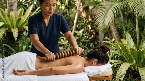 Woman receiving a relaxing back massage with a wooden roller in a tropical garden