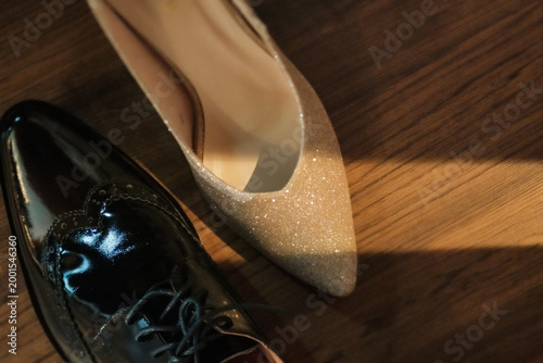 a pair of wedding shoes with one shoe from bridge and one shoe from groom on the wooden floor with light and shade from windows