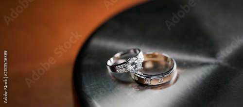 couple wedding rings put together on the black metallic stand on wooden table