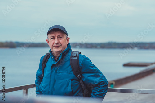 Smiling Senior Man in Blue Jacket and Cap by Riverside. Approachability and Well-being Concept