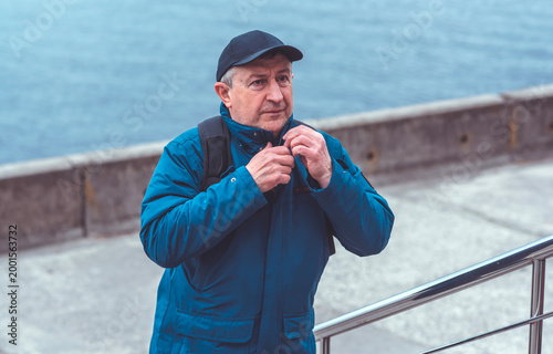 Smiling Senior Man in Blue Jacket and Cap by Riverside. Approachability and Well-being Concept