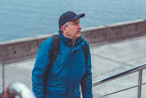 Smiling Senior Man in Blue Jacket and Cap by Riverside. Approachability and Well-being Concept