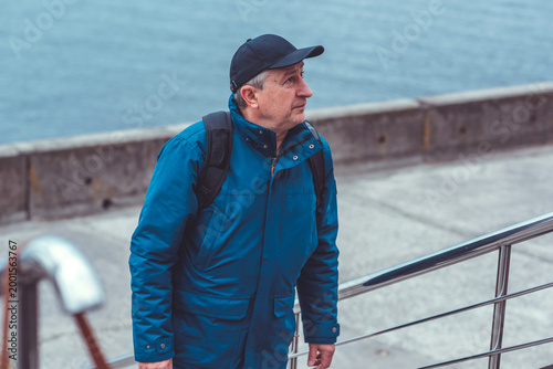 Smiling Senior Man in Blue Jacket and Cap by Riverside. Approachability and Well-being Concept