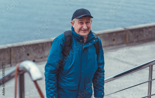 Smiling Senior Man in Blue Jacket and Cap by Riverside. Approachability and Well-being Concept