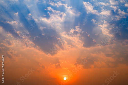sunset sky with dramatic sun rays crepuscular rays breaking through clouds in shades of orange and blue during golden hour for nature and inspiration background