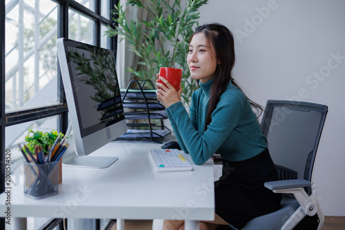 Asian woman taking coffee break at modern office desk