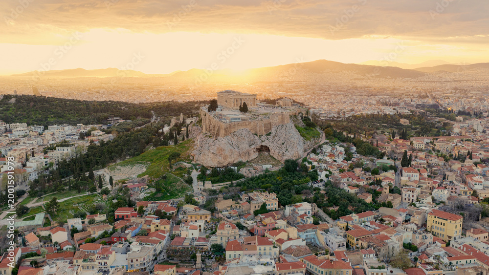 Fototapeta premium Ancient parthenon ruins crown the acropolis rock, overlooking athens as the setting sun bathes the cityscape in warm golden light, highlighting historic architecture and urban sprawl