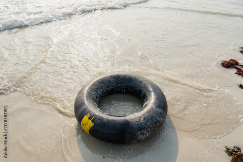 Canvas Print A Seaside Escape: A serene scene unfolds as a black inner tube rests on the edge of the shore, with gentle waves lapping at the sand, suggesting relaxation and carefree summer days