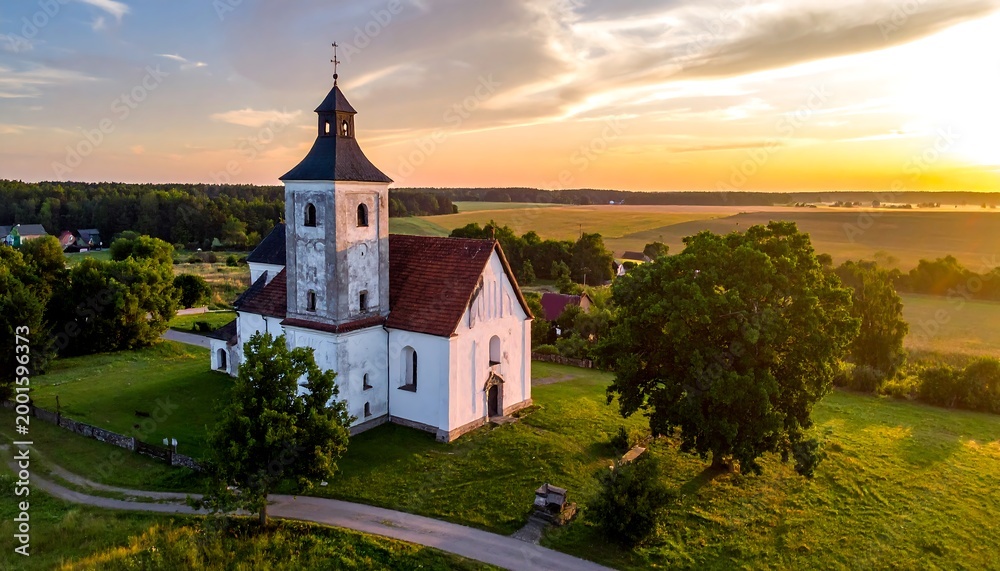 Naklejka premium Scenic drone view of church with tower in green landscape, sunset sky