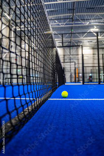 Tennis ball on a bright blue indoor padel court beside a black net