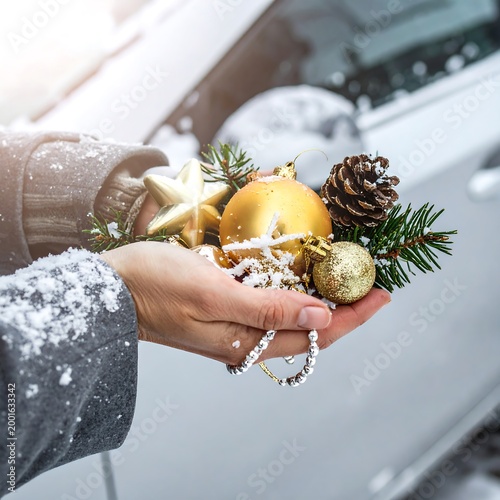 Snowy hand holding festive Christmas ornaments near a car in winter