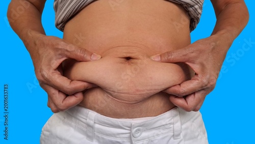 Woman with stomach pain, the fingers holding the flabbiness adipose sagging skin, large and overweight, flabby skin and cellulite on the body, belly fat and excess weight around the waist. 