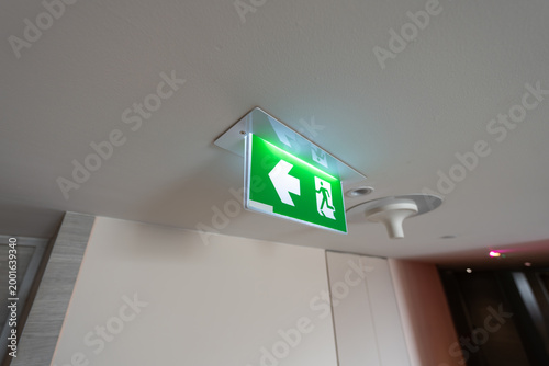 An emergency fire exit light box with arrow hangs from a hospital ceiling, combining evacuation drill concept with clear safety direction and escape guidance.