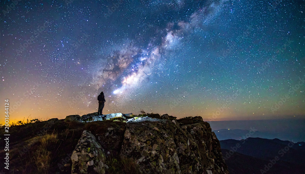 Fototapeta premium Witness a lone explorer on a rugged summit under a vibrant starry sky. This cinematic image captures the Milky Ways majesty, symbolizing wonder, discovery, and deep cosmic inspiration.
