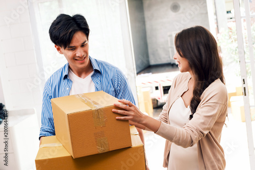 Smiling couple carrying cardboard boxes while moving into a bright home, helping each other with unpacking
