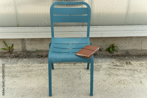Modern teal metal chair with a leather journal on the seat placed outdoors against a industrial wall