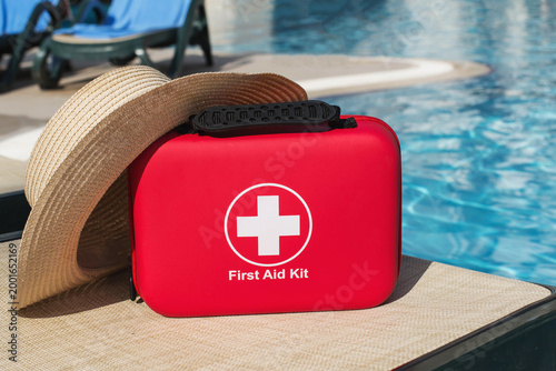 Poolside first aid kit with summer hat near resort water, vacation safety concept illustrating travel insurance, emergency preparedness, healthcare support, medicine assistance, 
