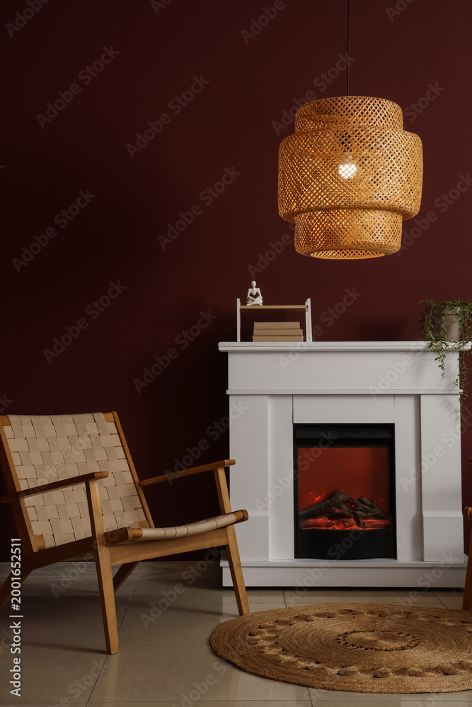 Obraz premium Interior of stylish living room with cozy armchair, fireplace and glowing lamp near red wall