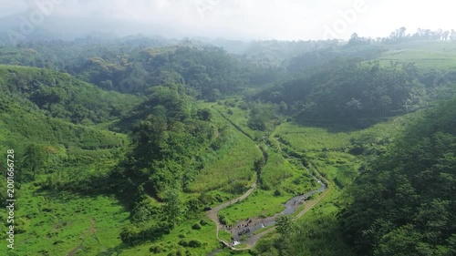 Aerial view of a lush green valley with a winding river and misty hills. Beautiful tranquil nature landscape drone footage.