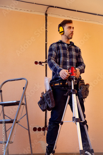 Worker uses laser level to prepare wall markings for chasing electrical system installation in construction interior work site