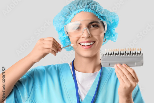 Female dentist with tooth color samples on light background, closeup