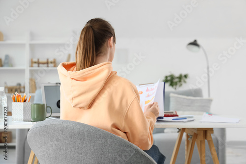 Teenage girl with diagrams working online at home, back view