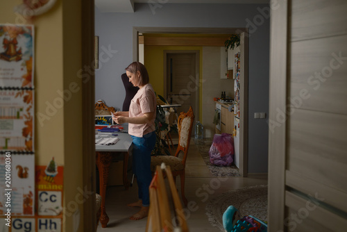 Woman sewing and crafting at a home table near a dress form in a lived-in apartment interior