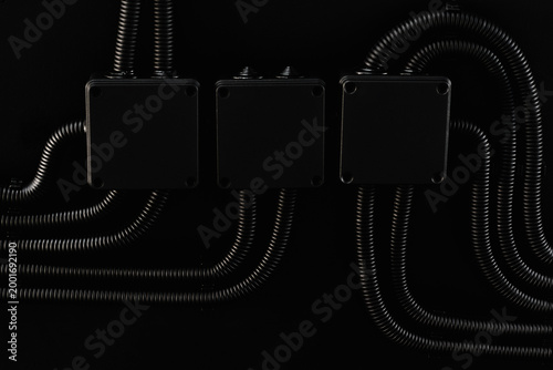 Boxes and electrical cable conduits hanging on black wall Industrial electrical conduits and junction boxes aligned on dark wall interior