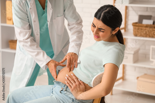 Female doctor examining young pregnant woman with pain in clinic