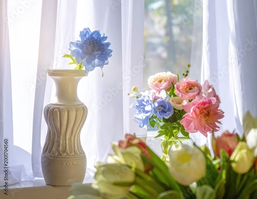 Several flower arrangements sit in vases near a bright, sunlit window
