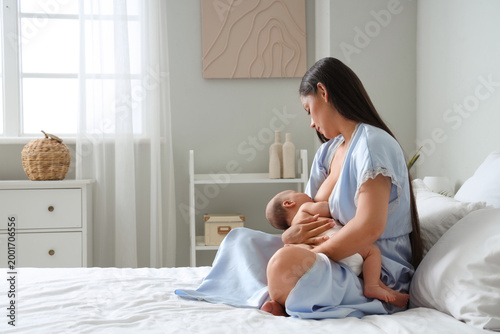 Beautiful young woman breastfeeding her baby in bedroom at home