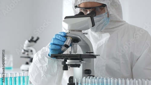 Tableau sur toile Medical virologist in protective hazmat gear examining viral samples under a mic