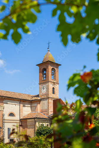 Bell tower with clock viewed through a frame of blurred green leaves in Grinzane Cavour, Italy