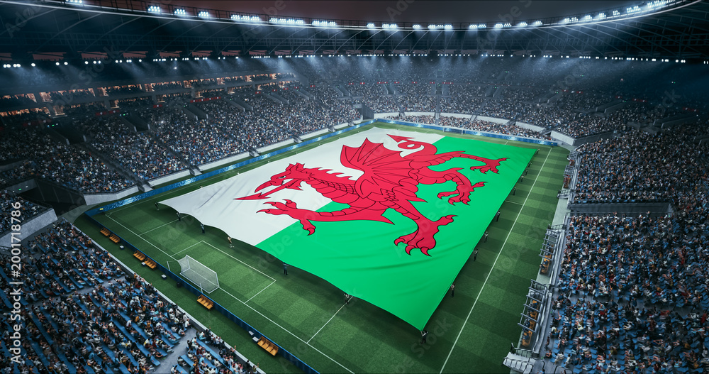 Fototapeta premium Professional Stadium Soccer Game Championship With Flag of Wales Spread Across the Pitch Before Football Match Start. Cheering Crowds of Fans Surround the Field. Aerial Wide Shot