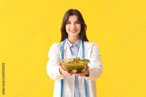 Female nutritionist with vegetable salad on yellow background