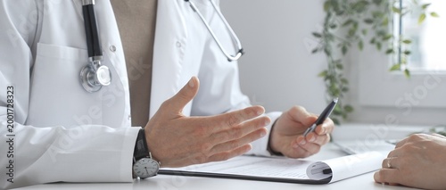 Fotografía Doctor man is explaining diagnosis to female patient during a medical consultation in a medical office, gesturing with hands over clipboard and white desk