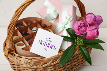 Wicker basket with candies, gifts and flowers for Mother's Day celebration on light wooden table, closeup