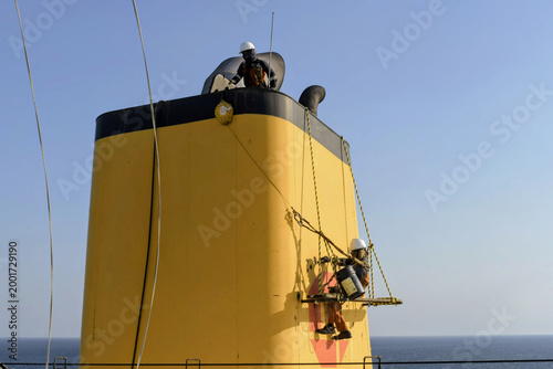 Fotografía seafarers carrying out maintenance and painting work on ship funnel using rope a