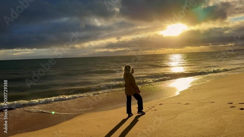 Woman holding mobile phone in hand and taking sunrise photo. Woman using smart phone take a photo at evening on the beach of sunset. Travel photo, copy space.