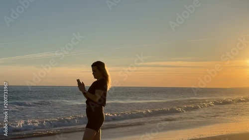 Vertical: Sunset, phone and beauty sexy woman taking a photo while traveling on the ocean or sea in tropical country. Smartphone, female tourist on vacation trip taking a picture 