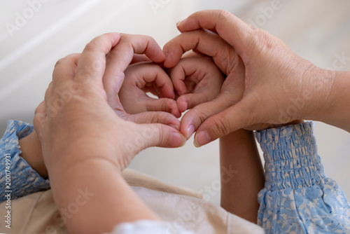 Fotografía Grandmother, mother and daughter form heart with hands, intergenerational connec