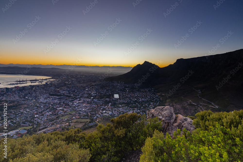Fototapeta premium An iconic blue hour and dawn seen from Lion's head over the skyline of Cape Town in South Africa with views on the spectacular and iconic Table mountain and Devil's head, while the sky shows its colou