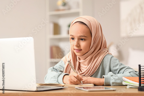 Little Muslim girl in hijab doing homework at home