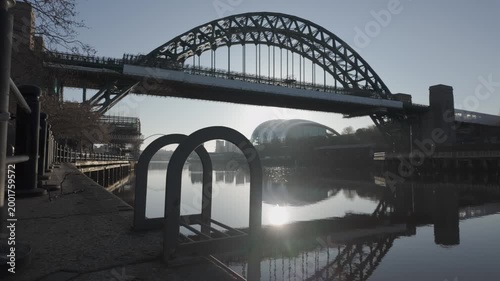 Cinematic low-level slide along the Newcastle quayside at dawn, featuring the iconic Tyne Bridge with the Glasshouse (Sage) and Millennium Bridge reflected in the river.
