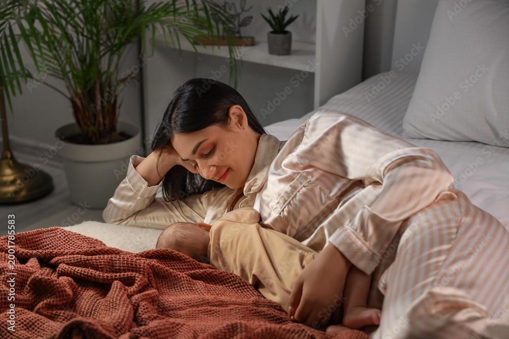 Fototapeta premium Young woman breastfeeding her baby in bedroom at night